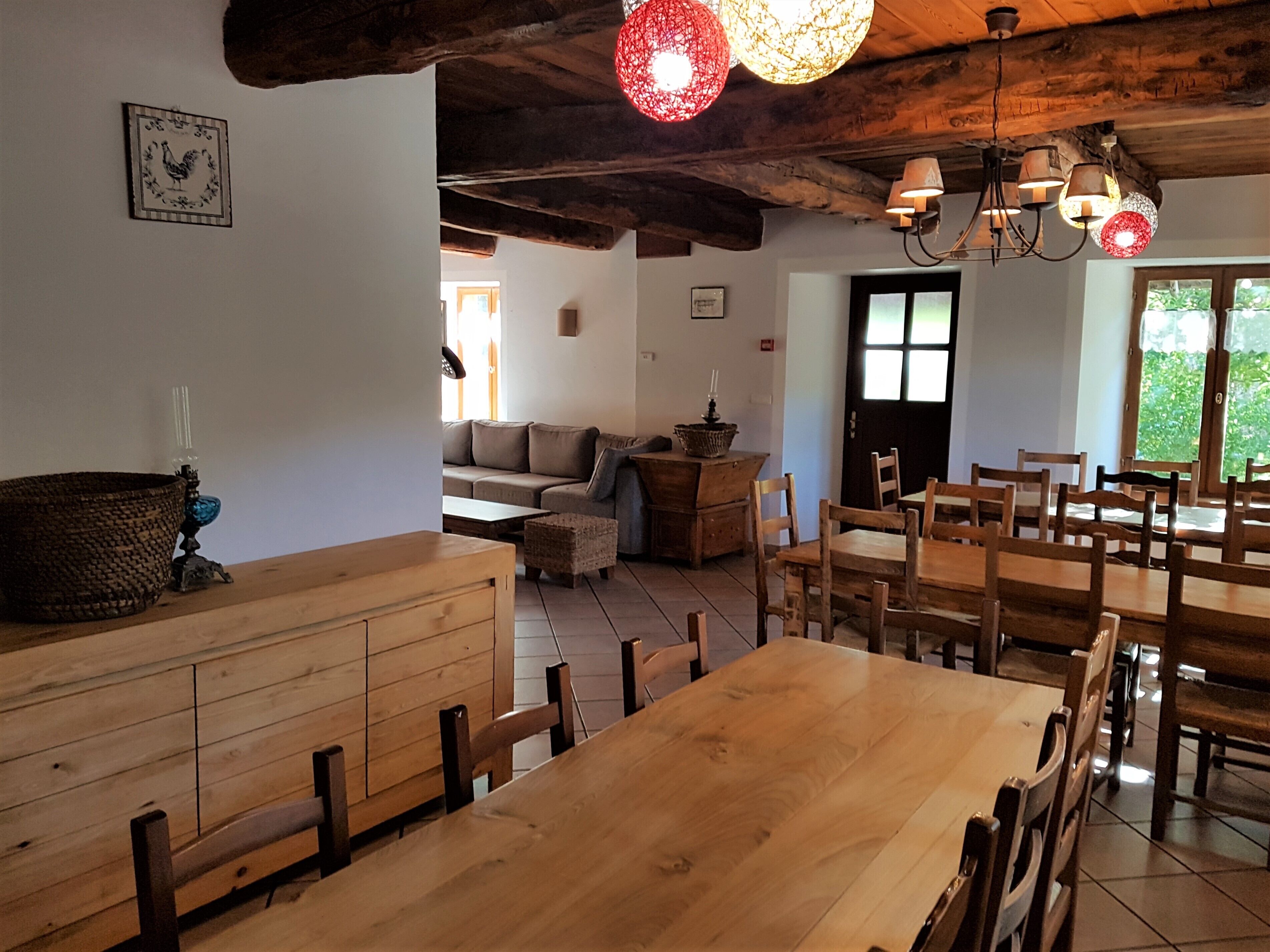 A rustic dining area with wooden furniture, a large table, and hanging red lights.