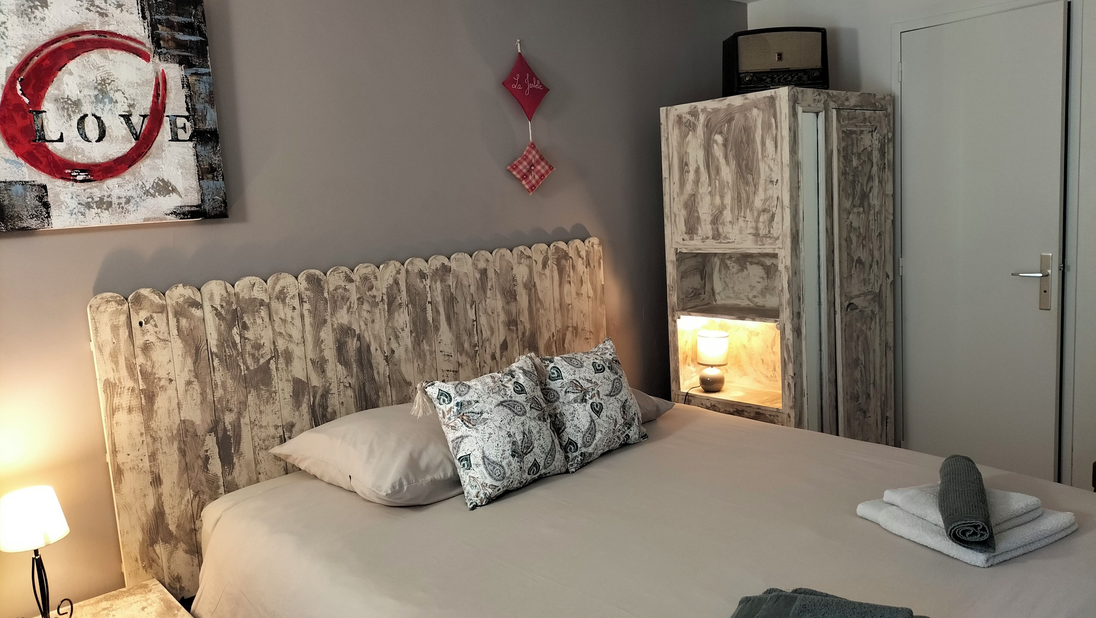 Une chambre à coucher comprenant un lit, une table de chevet, une lampe, une armoire et un élément de décoration murale.