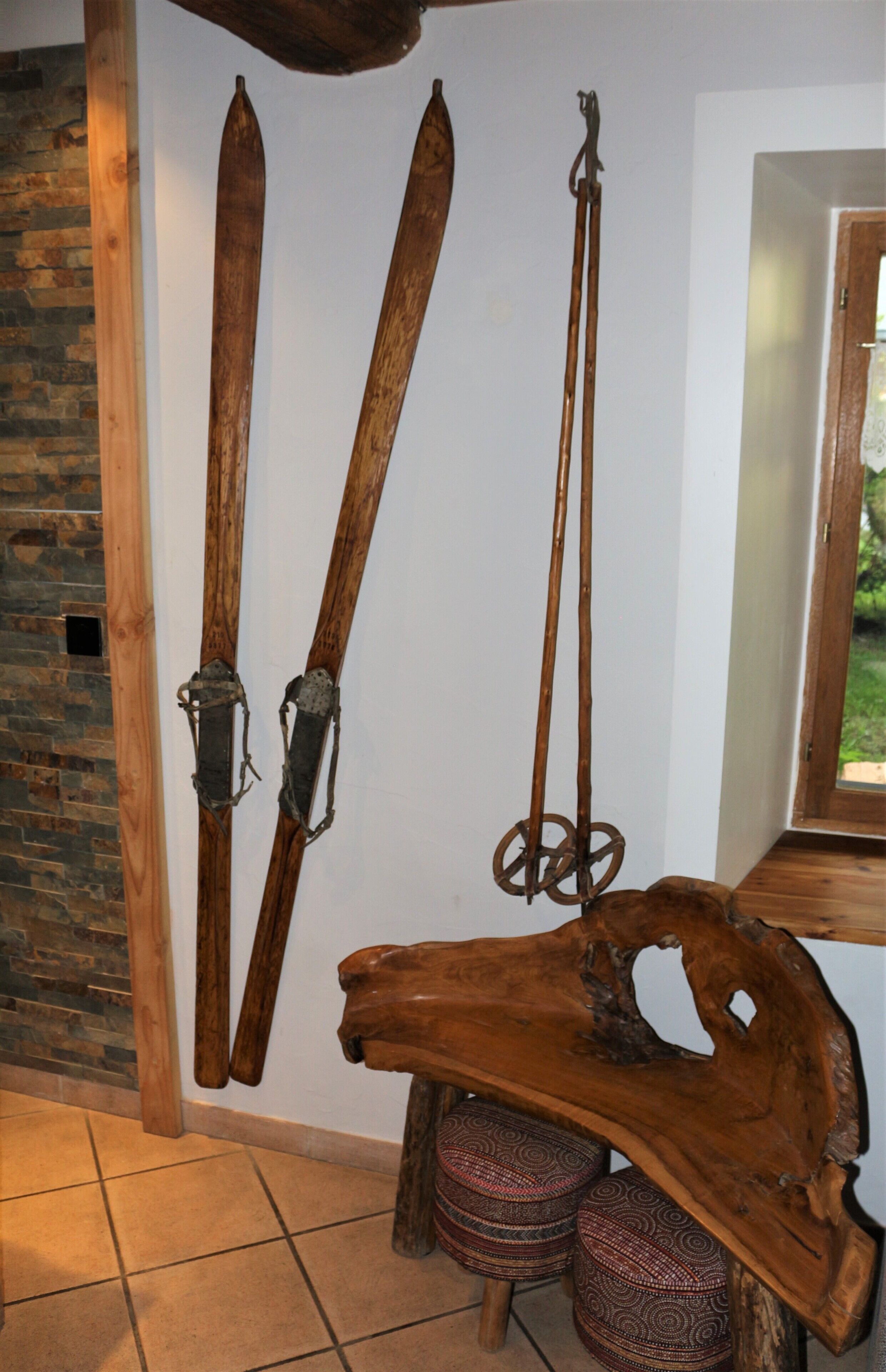 Esquíes y bastones de esquí de madera montados en una pared, un banco de madera y un otomano estampado.
