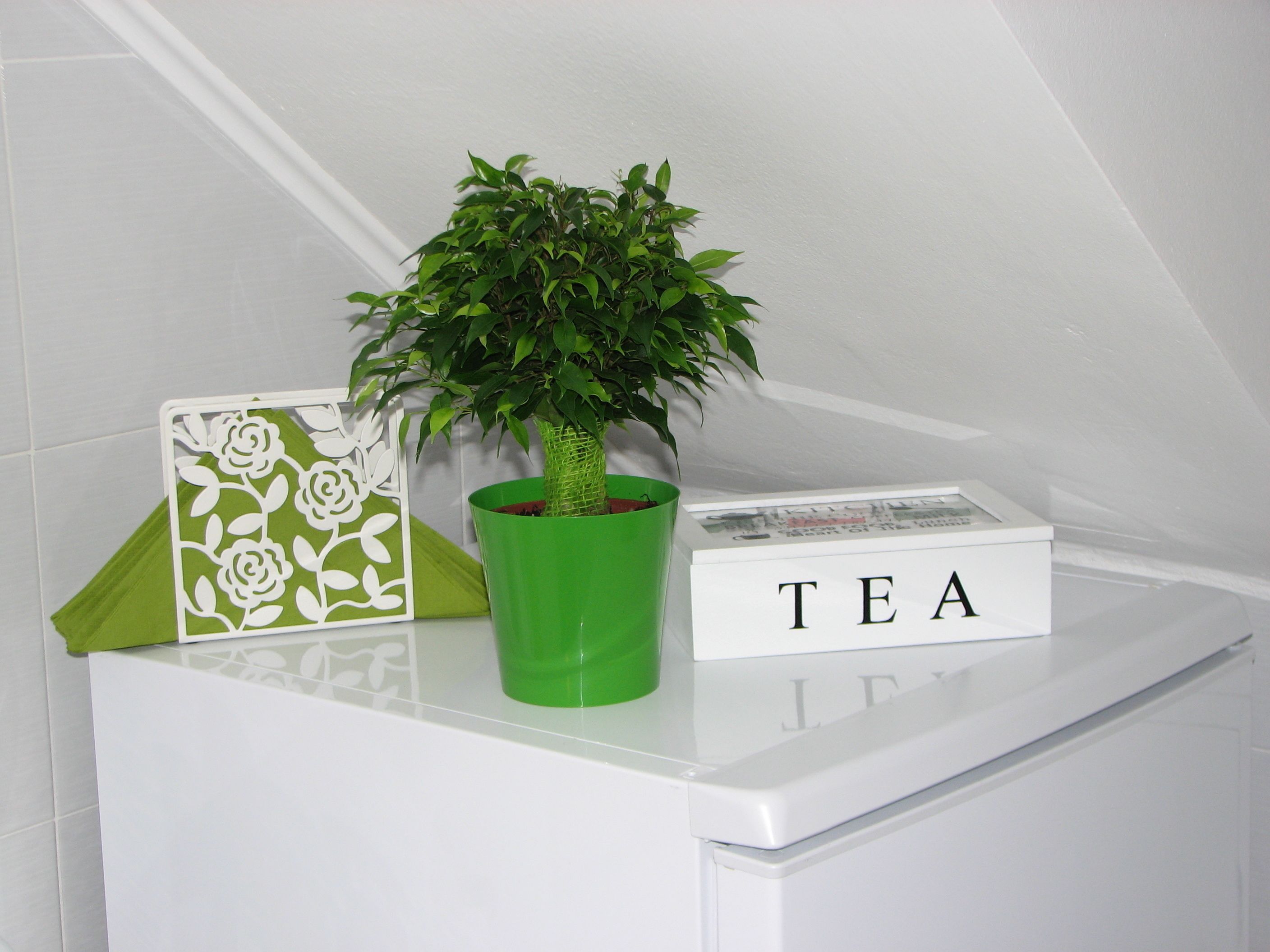 A white table with a green potted plant, a white box with the word "TEA" on it, and a white decorative item with a floral pattern.