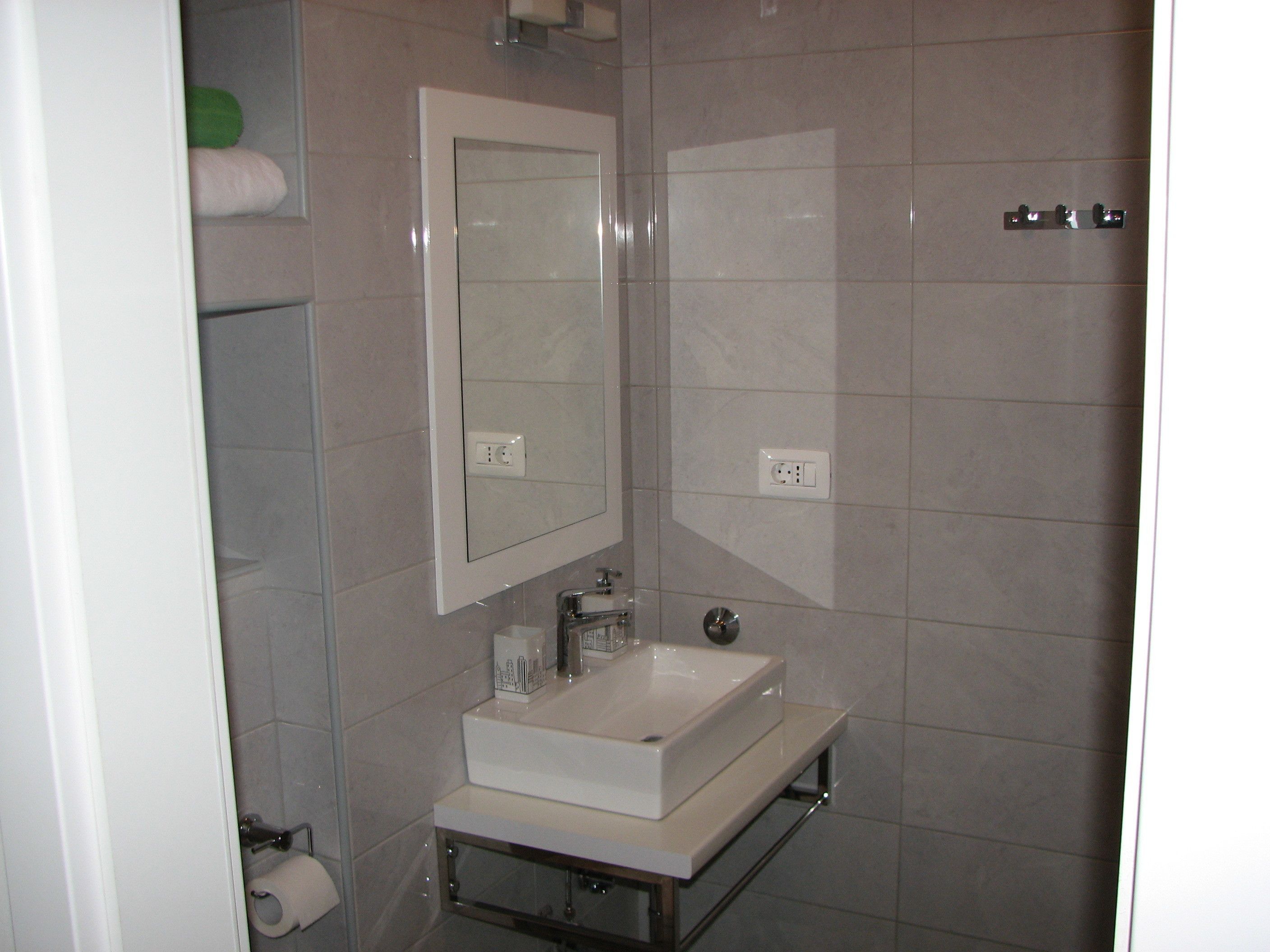 Une salle de bain avec un lavabo blanc, un miroir et un porte-serviettes. Il y a deux prises électriques sur le mur.