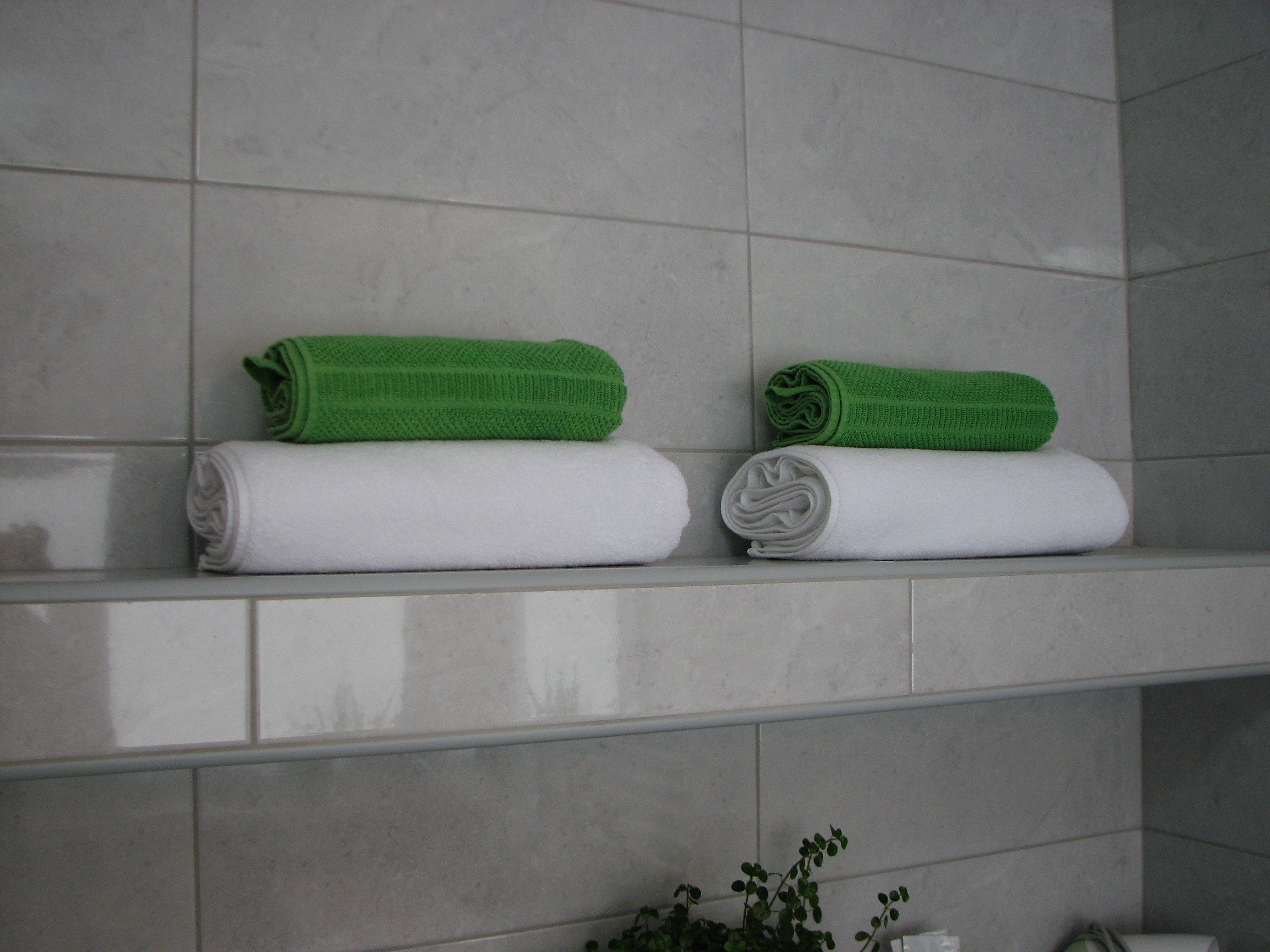 Two neatly folded towels, one green and one white, on a bathroom shelf.