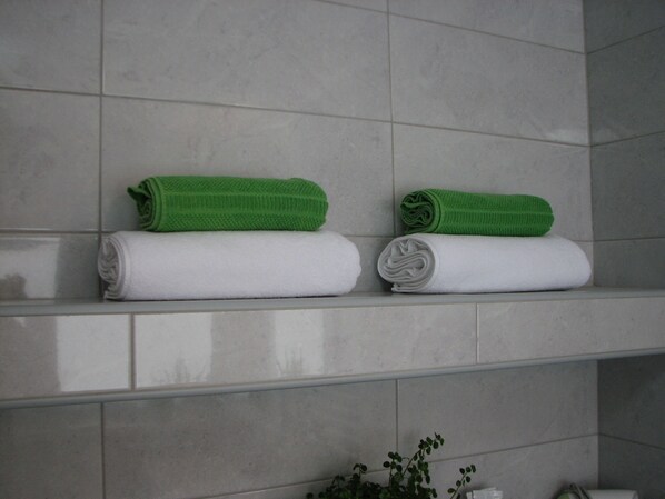 Two neatly folded towels, one green and one white, on a bathroom shelf. - Eva Luxury Rooms & Apartments (Plitvicka Jezera)