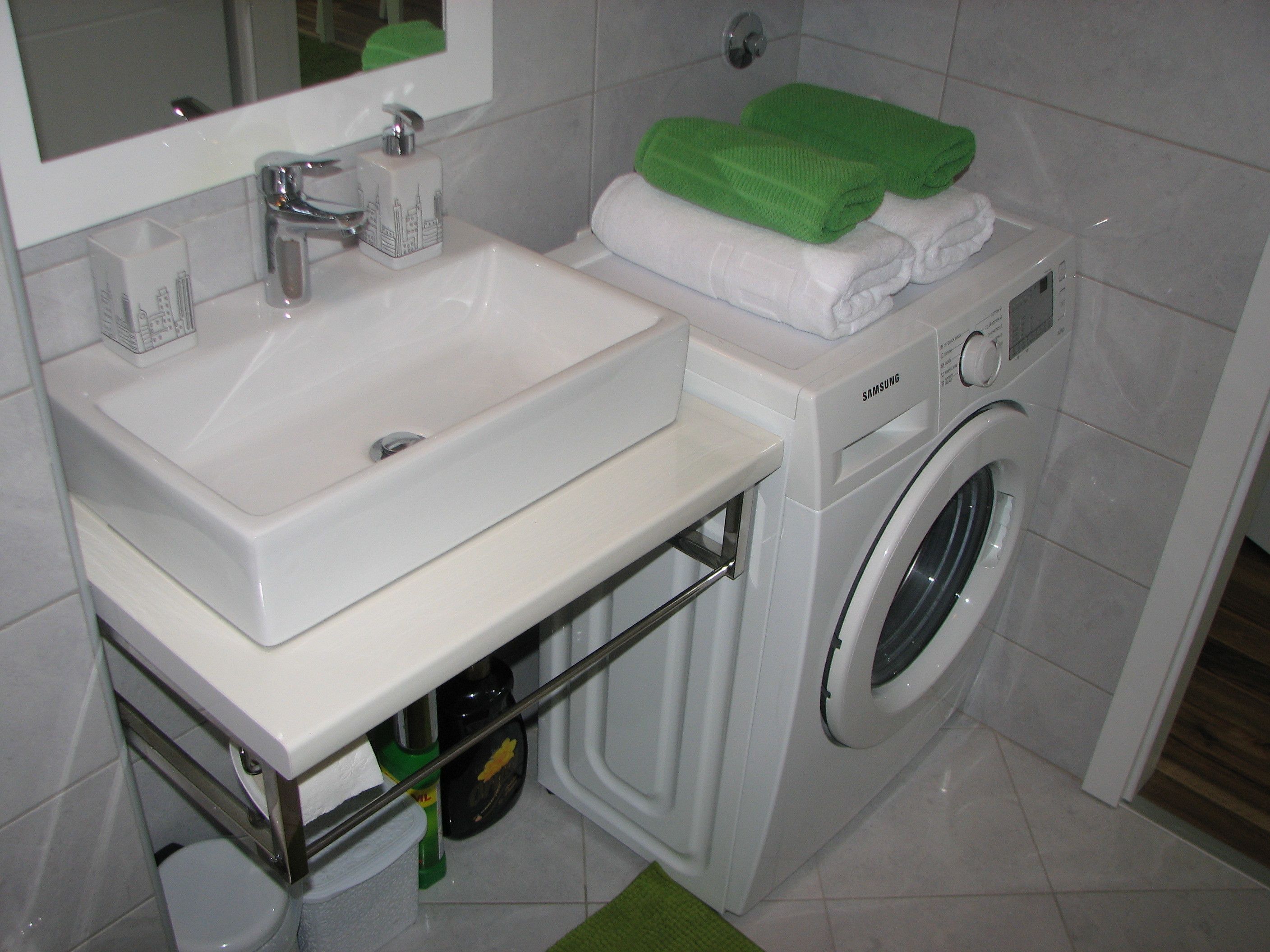 Un baño pequeño con un lavamanos blanco, una lavadora y un espejo sobre el lavamanos.