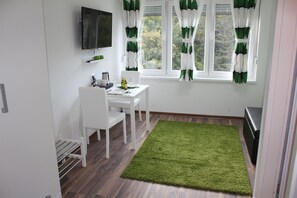 A small, clean room with a white desk, two chairs, a flat-screen TV mounted on the wall, and a window with green and white curtains. - Eva Luxury Rooms & Apartments (Plitvicka Jezera)