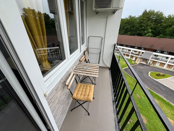 A balcony with a foldable table and chairs, a window with curtains, and a view of a residential area with a road and greenery. - Eva Luxury Rooms & Apartments (Plitvicka Jezera)