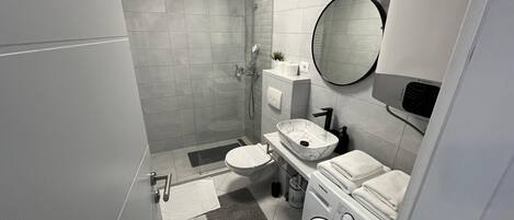 Un baño moderno con ducha a nivel del suelo, inodoro, lavamanos y lavadora.