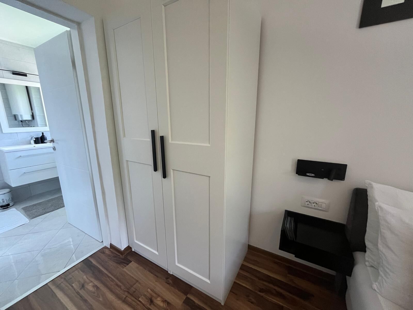 Een kamer met een witte inloopkast, een houten vloer, een wit wastafelmeubel en een zwart schap.