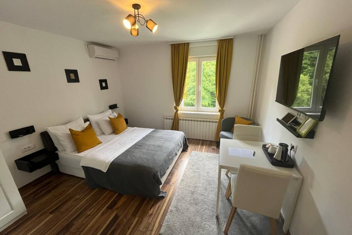 Hotellihuone, jossa on sänky, työpöytä, tuoli, televisio ja ikkuna, jossa on verhot.
