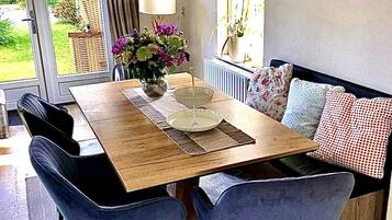 Een eetgedeelte met een houten tafel, twee blauwe stoelen, een bloemenvaas en een schilderij aan de muur.