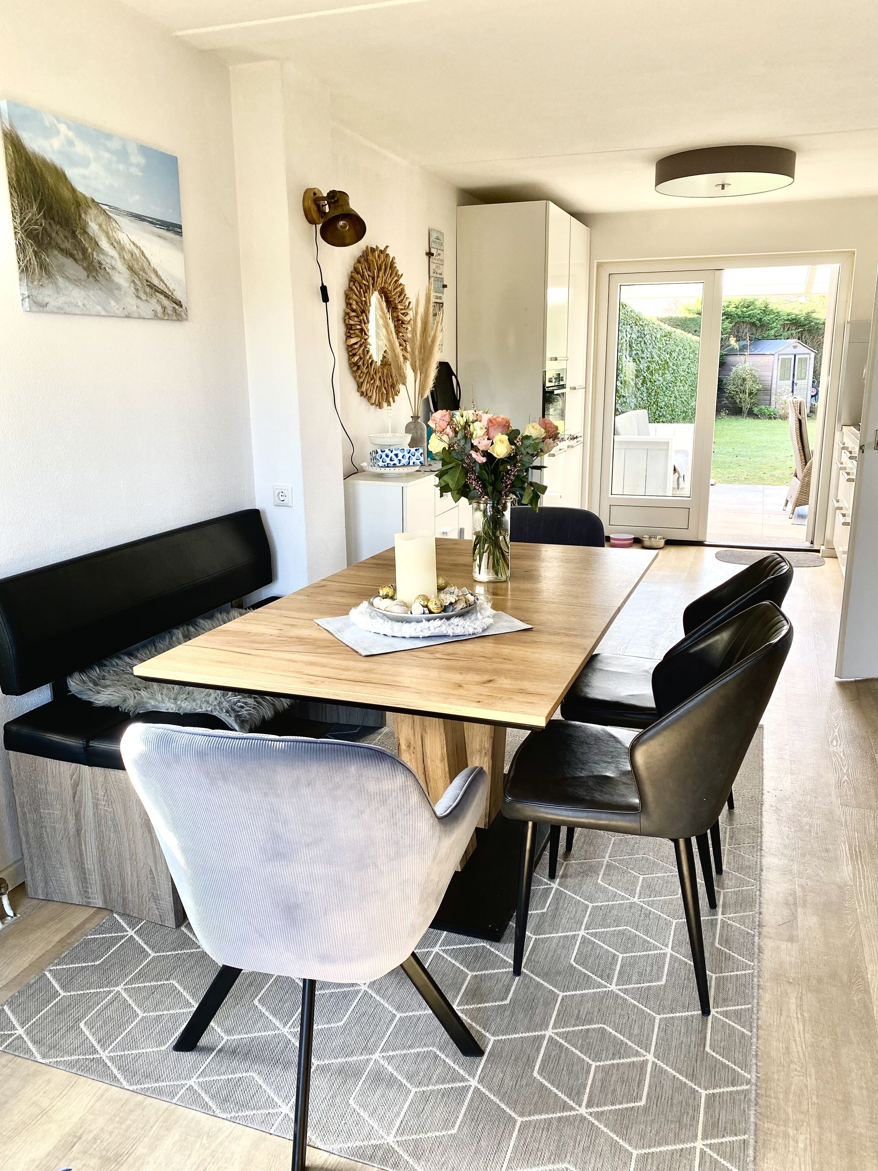 A dining area with a wooden table, black and grey chairs, a vase with flowers, and a painting on the wall.
