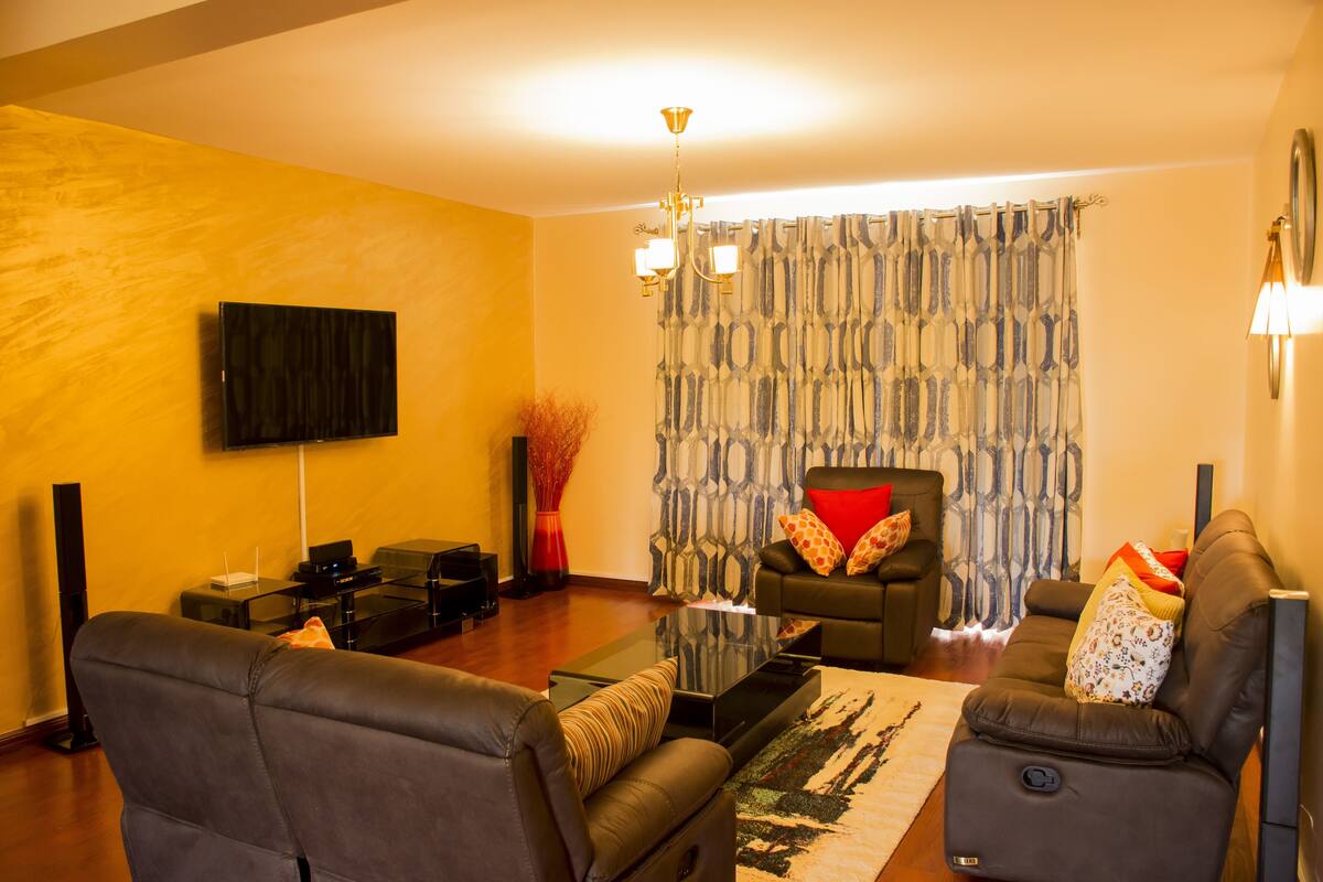 Una sala de estar moderna con un televisor de pantalla plana montado en la pared, un conjunto de sofás, una mesa de centro y una cortina estampada.