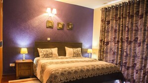 Ein Schlafzimmer mit einem großen Bett, zwei Nachttischen mit Lampen, einer Wandleuchte und einem Vorhang mit Marmormuster.