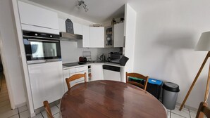 A compact kitchen with white cabinets, a built-in oven, a sink, and a dining table with chairs. - Cozy 1BR Apartment with Terrace, 200m from Sandy Beach (Les Sables-d'Olonne)