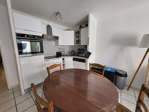 A compact kitchen with white cabinets, a built-in oven, a sink, and a dining table with chairs.