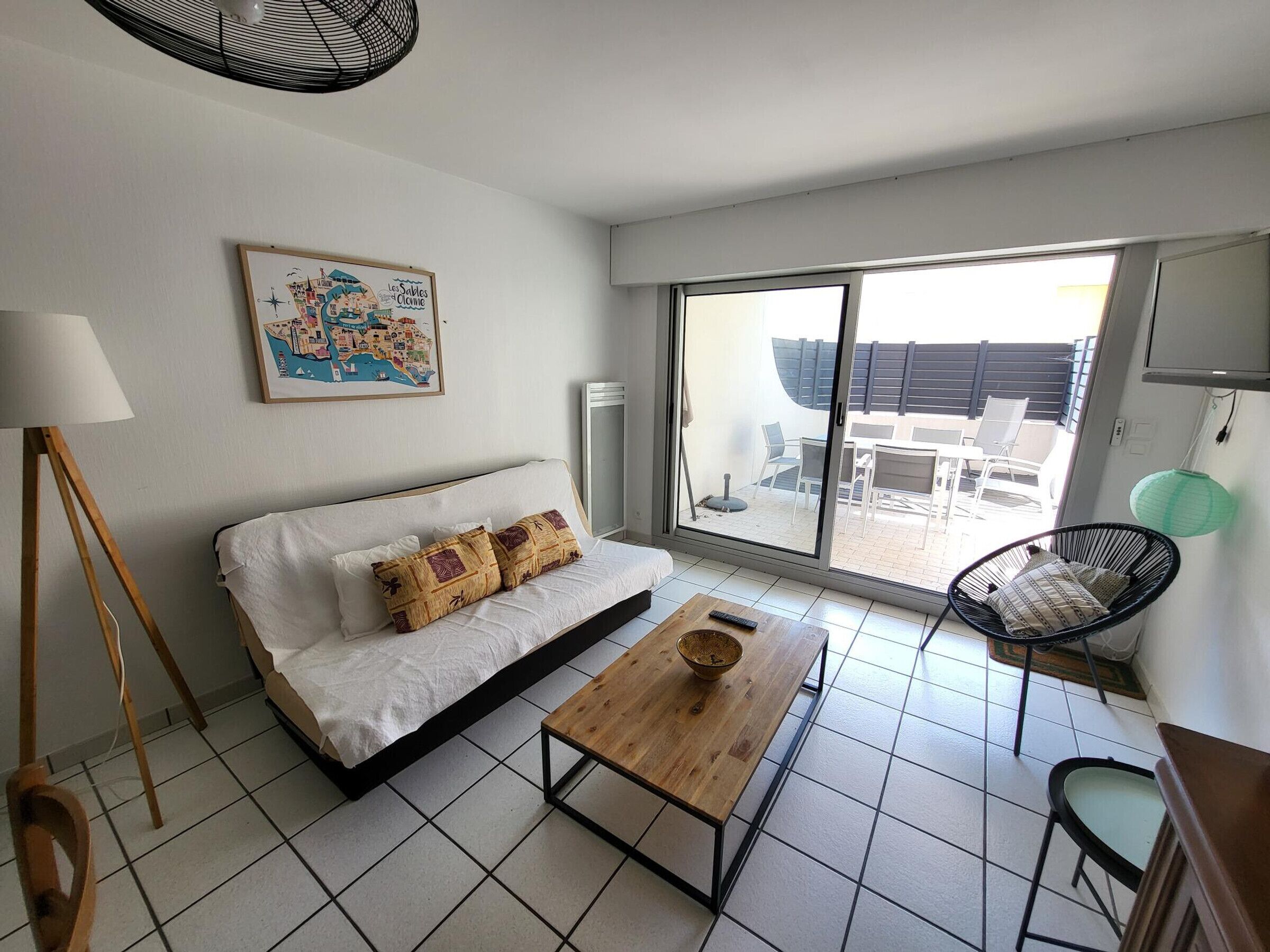 A modern room with a bed, a wooden table, a chair, a floor lamp, and a large window.