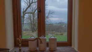 A kitchen sink with a faucet, three white containers with handles, and a window with a view of a tree and a cloudy sky. - Tanglewood Barn (Carlisle)