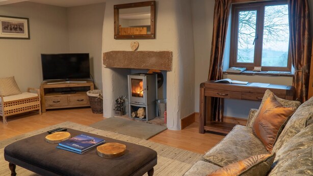 A cozy living room with a fireplace, a television, a sofa, and a desk with a window. - Tanglewood Barn (Carlisle)