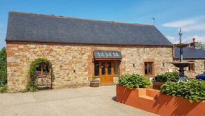 A stone building with a wooden door, a small window, and a fountain in the garden. - Tanglewood Barn (Carlisle)