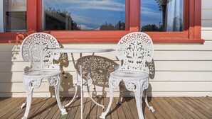 Two ornate white metal chairs and a small table set on a wooden deck in front of a building with a red window frame. - Settle In Retro cottage, Cowes family holiday 10 min walk to beach, FREE WIFI (Cowes)