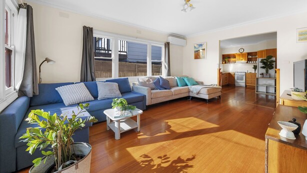 A living room with a blue sofa, a grey sofa, and a white armchair. There is a small white table with a plant. A kitchen is visible in the background. - Settle In Retro cottage, Cowes family holiday 10 min walk to beach, FREE WIFI (Cowes)