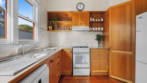 A kitchen with wooden cabinets, a stove, a sink, and a clock on the wall. - Settle In Retro cottage, Cowes family holiday 10 min walk to beach, FREE WIFI (Cowes)