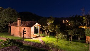 Un bâtiment rustique en briques, doté d’un petit porche, entouré de verdure et surplombant un ciel nocturne dégagé.