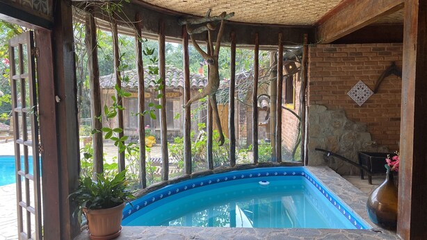 Un espace piscine avec un bord carrelé de bleu, entouré de poutres en bois et d’un mur en briques.