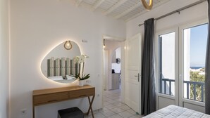 A modern bedroom with a large bed, a bedside table with a mirror, and a view of the outdoors through a sliding door. - Secret Garden Apartments (Mykonos)