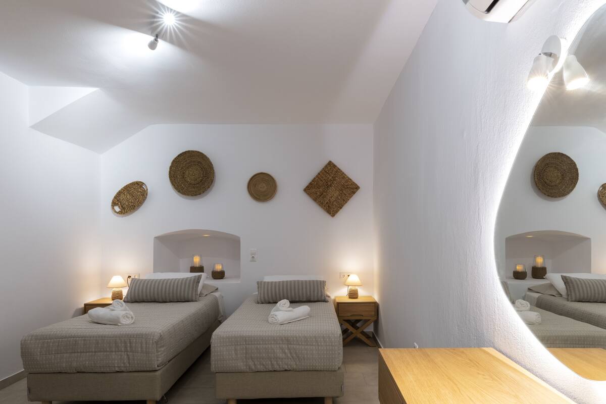 A modern, minimalist bedroom with two beds, a wooden table, and wall-mounted lamps.