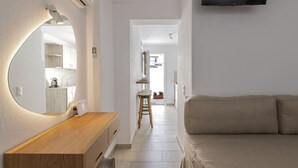 A modern hotel room with a wooden vanity, a large mirror, a beige sofa, and a flat-screen TV mounted on the wall. - Secret Garden Apartments (Mykonos)