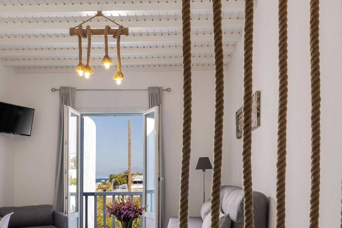 A modern living room with a sofa, a small table with a vase, and a balcony with a view.