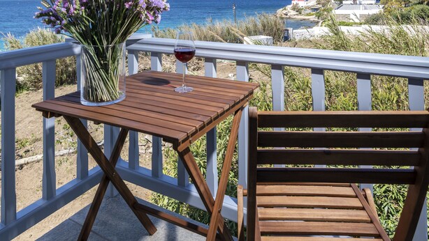 A wooden table and chair on a balcony with a view of the ocean. - Secret Garden Apartments (Mykonos)