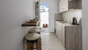 A narrow kitchen with wooden cabinets, a countertop, and a bar stool area. - Secret Garden Apartments (Mykonos)