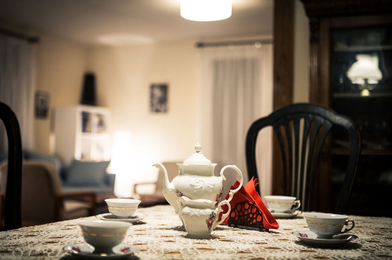 Uma mesa de jantar com um bule branco, xícaras e um guardanapo vermelho.