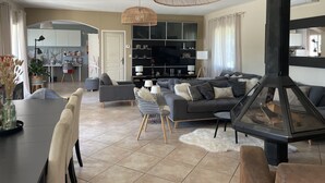 Un salon moderne avec une cheminée, des canapés gris, une table à manger et une cuisine en arrière-plan.