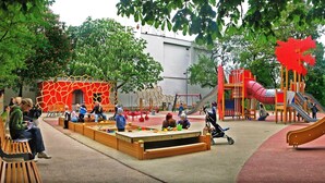 Ein Spielplatz mit verschiedenen Spielgeräten, darunter Rutschen und Kletterbereichen, umgeben von Bäumen und Bänken.
