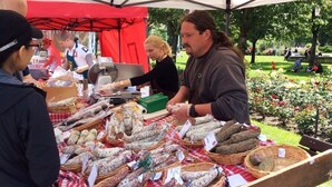 Ein Marktstand mit verschiedenen Wurstsorten, präsentiert auf einem Tisch unter einer roten Markise.