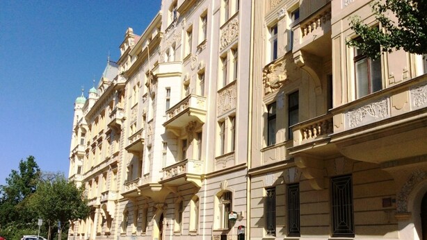 Eine Reihe geparkter Autos entlang einer Straße, mit einem Gebäude, das klassische Architektur mit aufwendigen Balkonen und Zierleisten aufweist.
