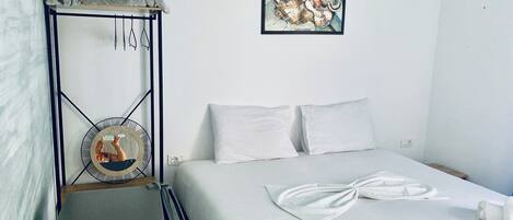 Une chambre d’hôtel avec un lit, une petite table sur laquelle est posée une serviette, une œuvre d’art accrochée au mur et une prise électrique.