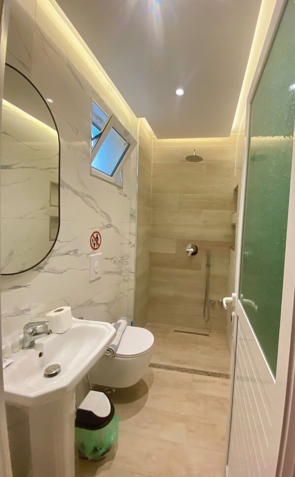 A modern bathroom with a marble sink, a toilet, and a glass-enclosed shower.