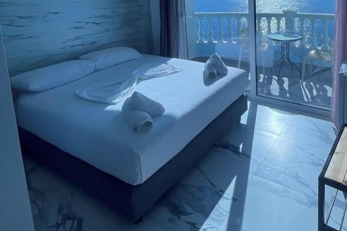 A bedroom with a bed, a small table, and a view of the sea through a balcony.