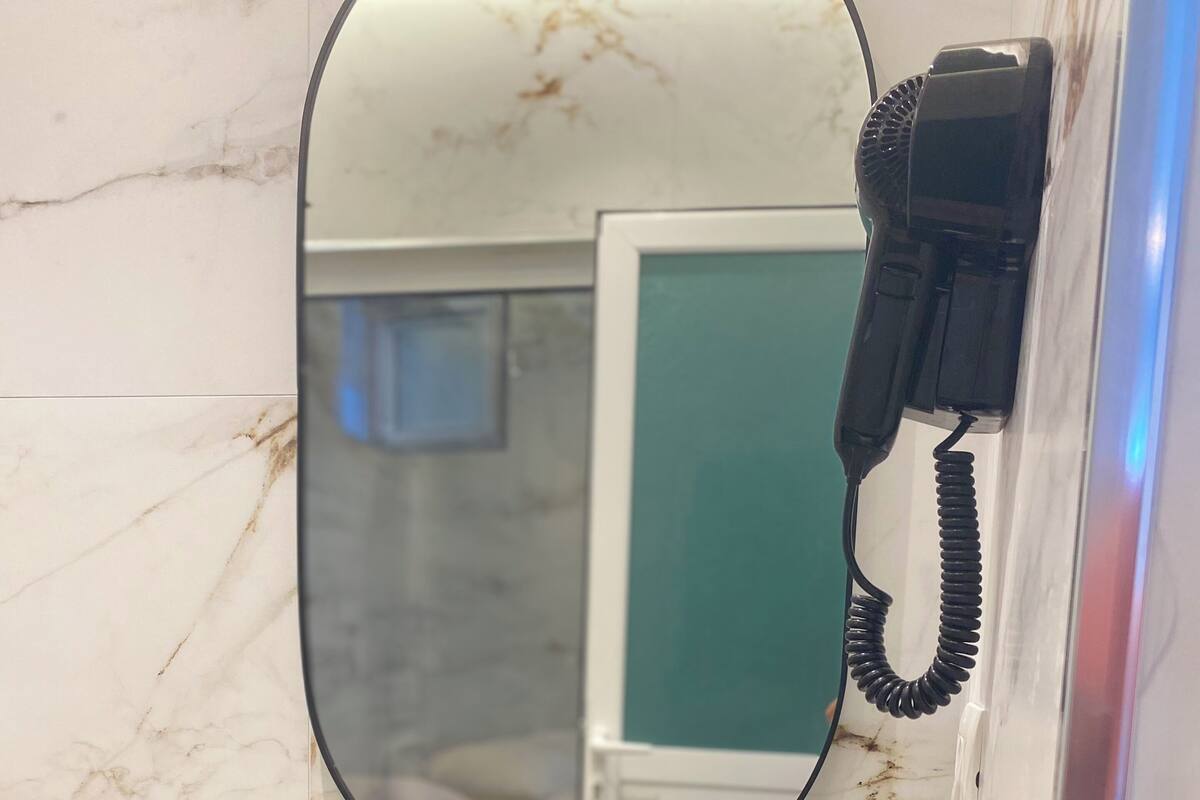 A bathroom sink with a mirror, a hairdryer, and toiletries.