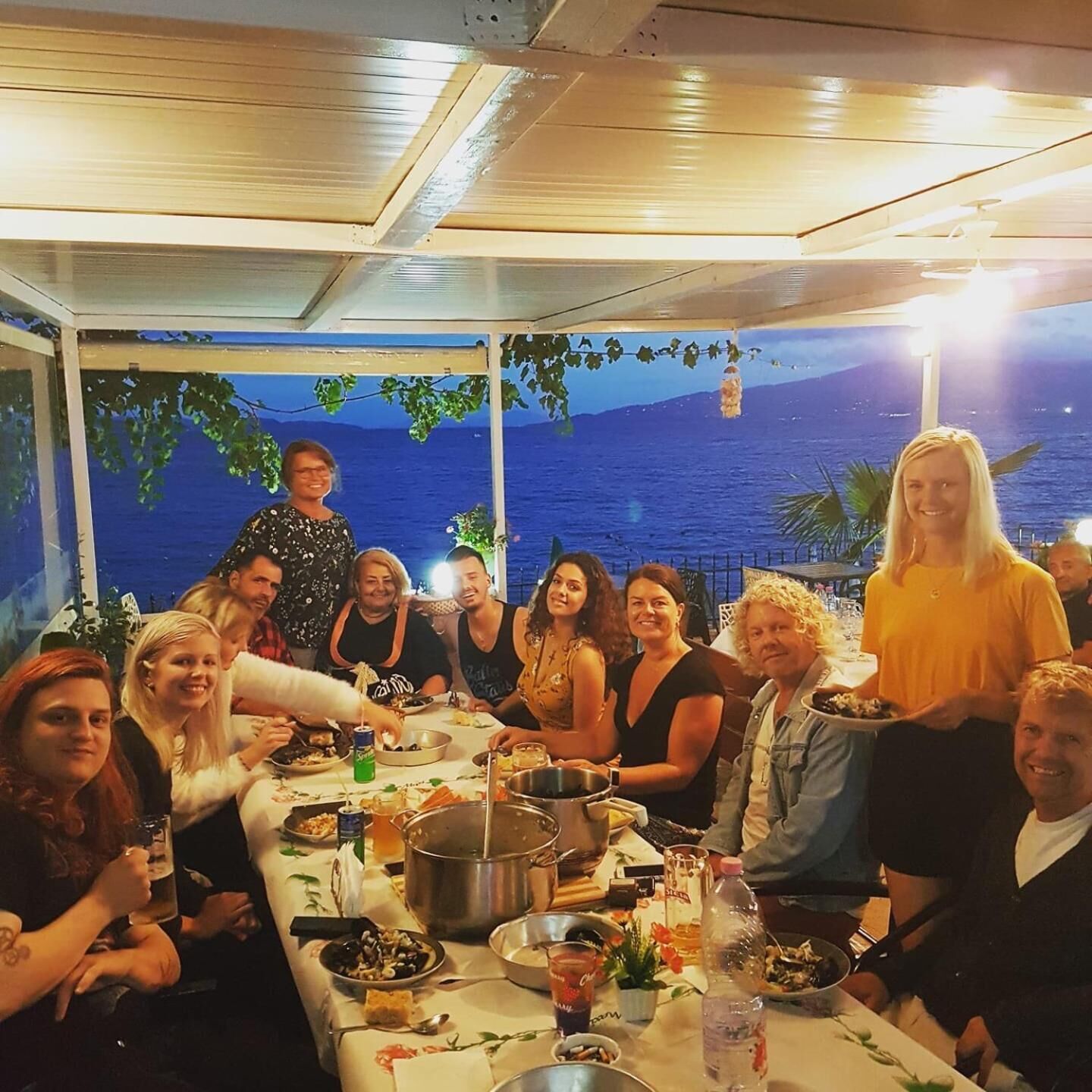 Een groep mensen dineert aan een buitentafel met uitzicht op zee.