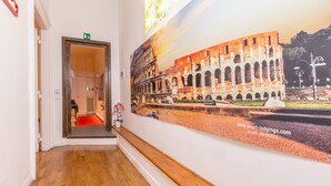 A hallway with a wooden floor, a door leading to a room, and a large poster of the Colosseum.