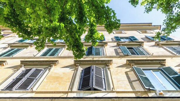A building facade with multiple windows and shutters, likely a hotel or apartment building.