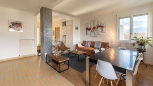 Ein modernes Wohnzimmer mit einem braunen Sofa, einem Esstisch mit Stühlen, einem Couchtisch und einem großen Fenster mit Blick.