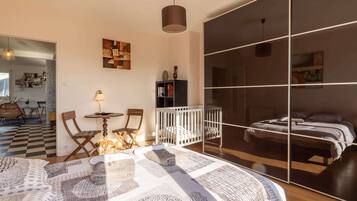 Een moderne slaapkamer met een groot bed, een ledikant, een zithoek met stoelen en uitzicht door een schuifdeur.