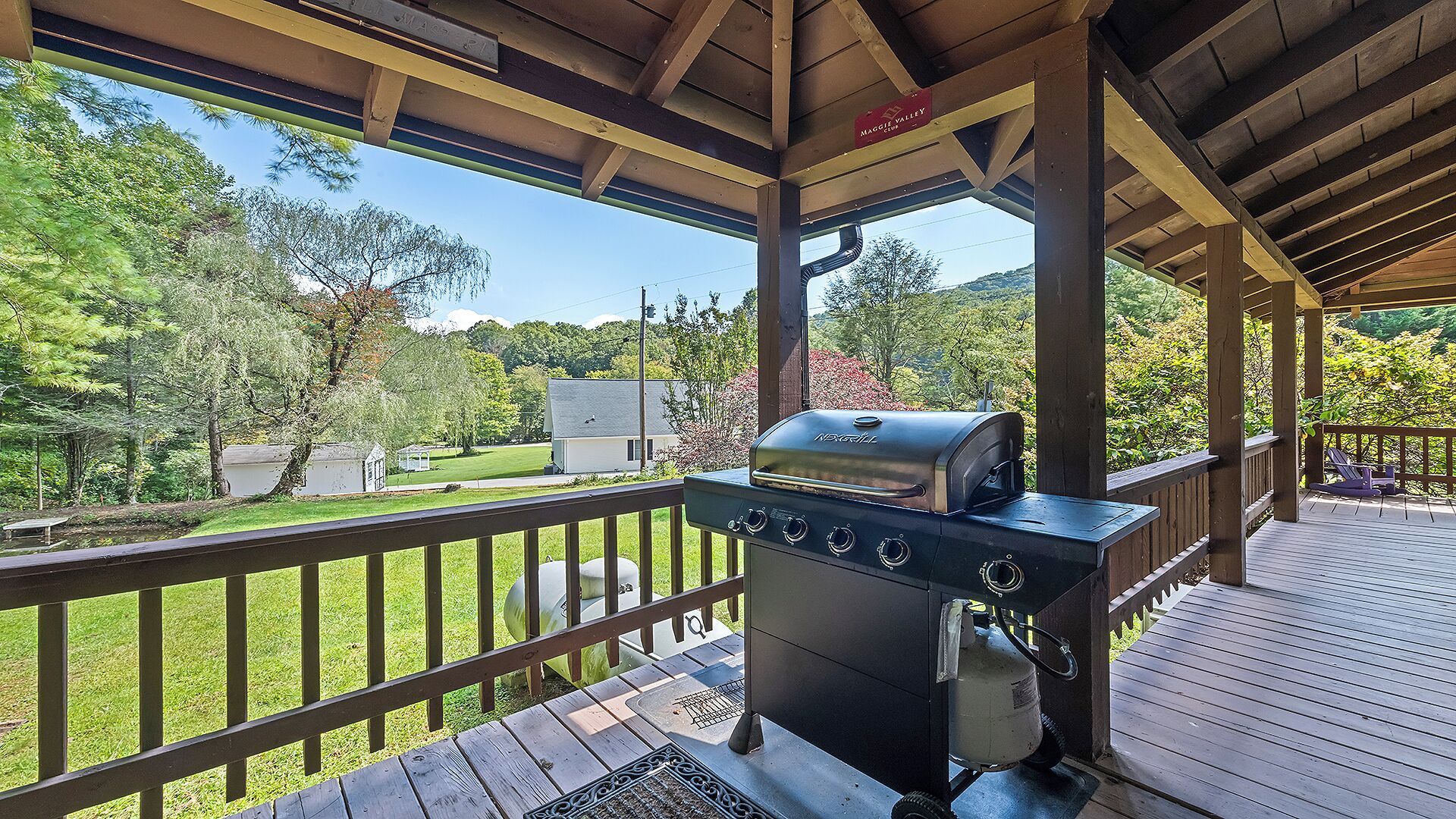 Un espace extérieur abrité, doté d’un barbecue et offrant une vue sur une pelouse et des arbres.