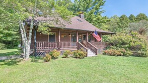 A wooden cabin with a porch, a flag, and a chimney. - 2BD 2BA Cozy Log Cabin, Easy Paved Access, View, Gas Log, Hot Tub, Wifi Pond (Waynesville)